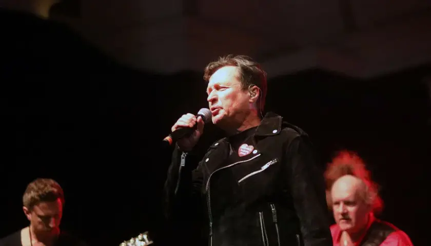Kawalec śpiewa, a budka suflera czuwa. Muzycy na scenie, w tle gitara i czerwona koszula.