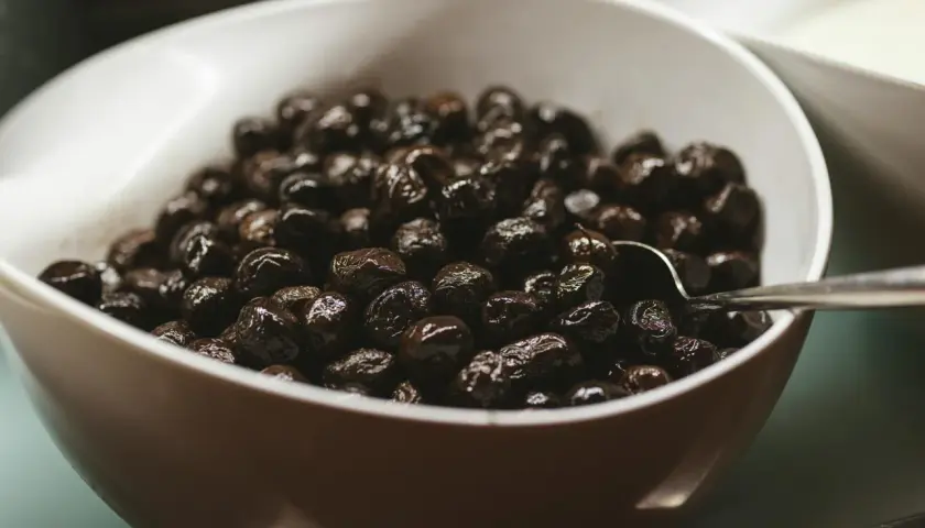 Un cuenco blanco lleno de aceitunas negras brillantes, perfecto para tus recetas con aceitunas negras.
