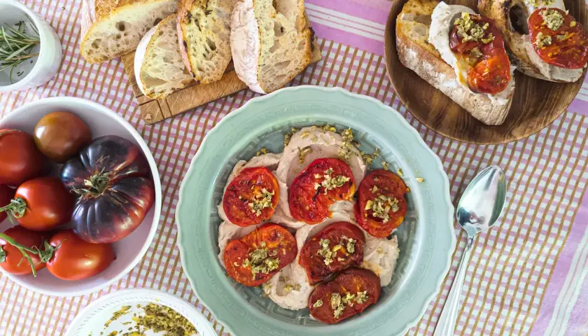 Tomates italianos asados sobre una crema suave, acompañados de pan rústico y tomates frescos.
