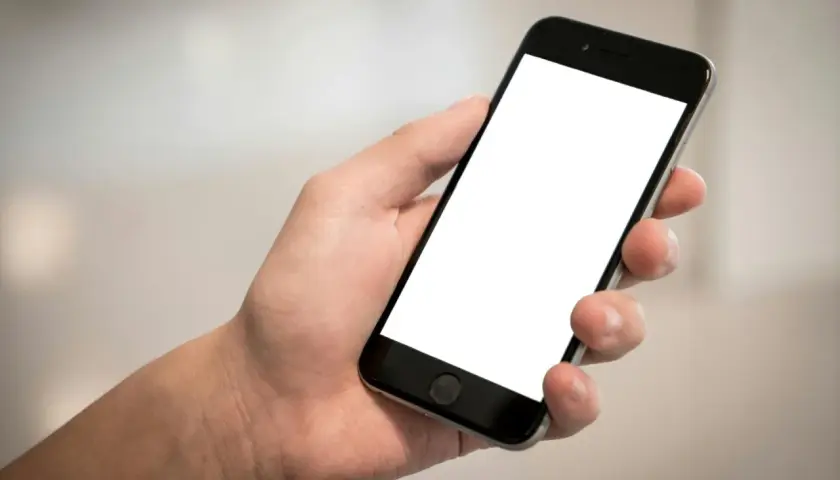 Dłoń trzyma smartfon z pustym ekranem, idealny do pokazania szybkich odpowiedzi SMS, przykładów komunikacji.