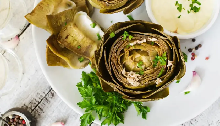 Deliciosas alcachofas al horno, tiernas y doradas, servidas con una cremosa salsa y perejil fresco. Un plato perfecto para disfrutar.