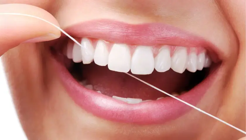 Dita che usano il filo interdentale per pulire i denti bianchi e perfetti. Un gesto quotidiano per un sorriso smagliante.