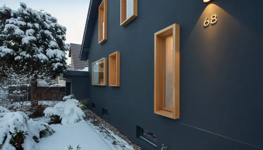 Modernes Haus mit Holzfenstern im Schnee. Ein Architekt hat hier mit klaren Linien und Kontrasten gebaut.