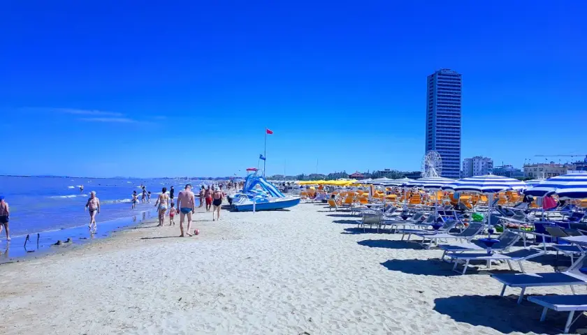 Plage animée à Cesenatico, Italie, avec des parasols rayés, des chaises longues et des baigneurs profitant du soleil sous un ciel bleu éclatant.