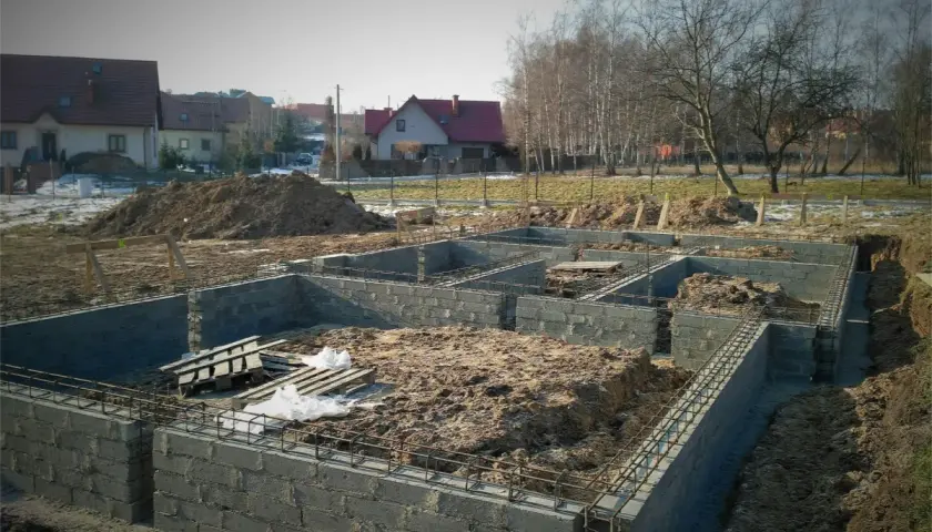 Budowa fundamentów domu w trakcie. Widać zbrojenie i bloczki betonowe, przygotowywane pod izolację poziomą fundamentów.