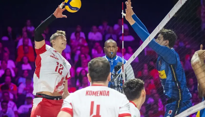 Siatkarz w biało-czerwonej koszulce z numerem 12 atakuje piłkę, podczas gdy zawodnik w niebieskiej koszulce z Włoch próbuje ją zablokować. Polska kontra Włochy na boisku.