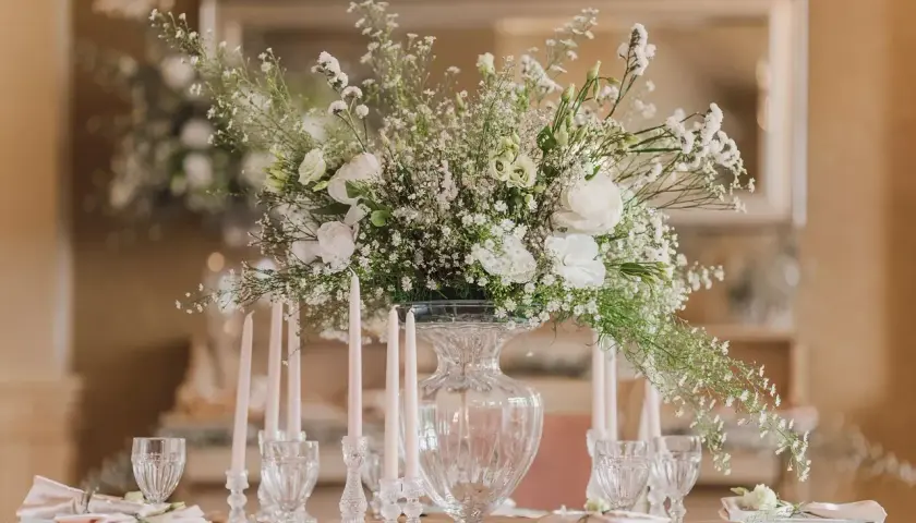 Une élégante composition florale blanche trône sur une table dressée, entourée de bougies fines et de verres ciselés.