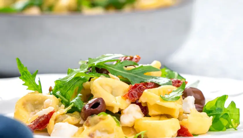Ein Teller mit Tortellinisalat mit Rucola, sonnengetrockneten Tomaten und Oliven.
