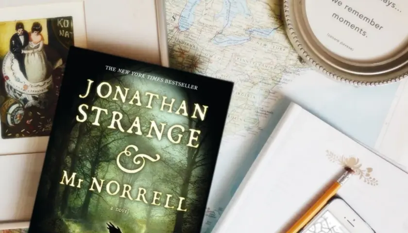 Książka "Jonathan Strange i Pan Norrell" leży obok mapy, telefonu i okularów, gotowa na podróż pełną magii.