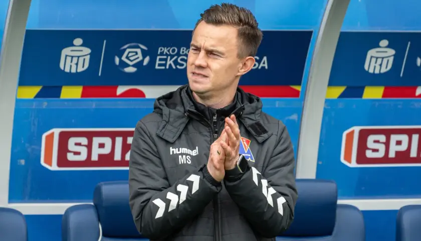 Trener z PKO BP Ekstraklasa w TVP, kiedy? Mężczyzna w kurtce z logo "hummel" klaszcze na ławce rezerwowych.