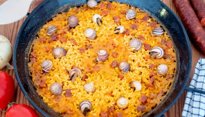 Arroz con caracoles, un plato tradicional español, se presenta en una paellera, adornado con caracoles y trozos de chorizo.