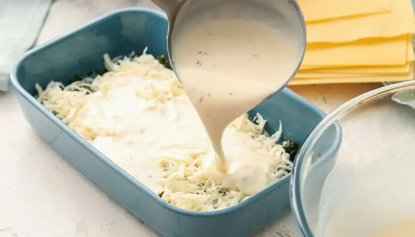 Se vierte bechamel para lasaña sobre queso rallado en un molde azul.