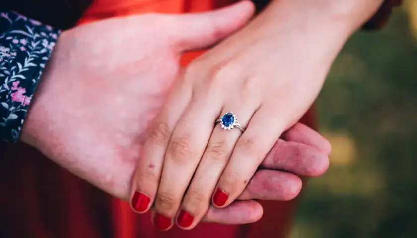 Ein Ring mit einem tiefblauen Saphir und kleinen Diamanten, gehalten von zwei Händen.