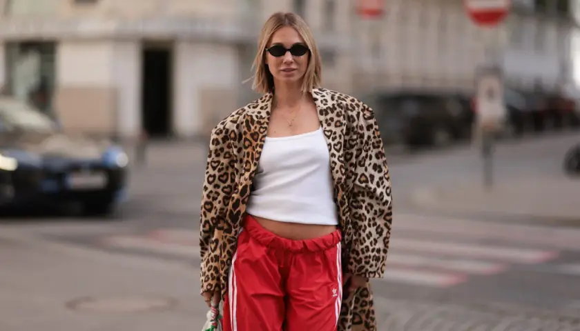 Kobieta w panterkowym płaszczu i czerwonych spodniach dresowych Adidas. Inspiracja na adidas samba stylizacje.