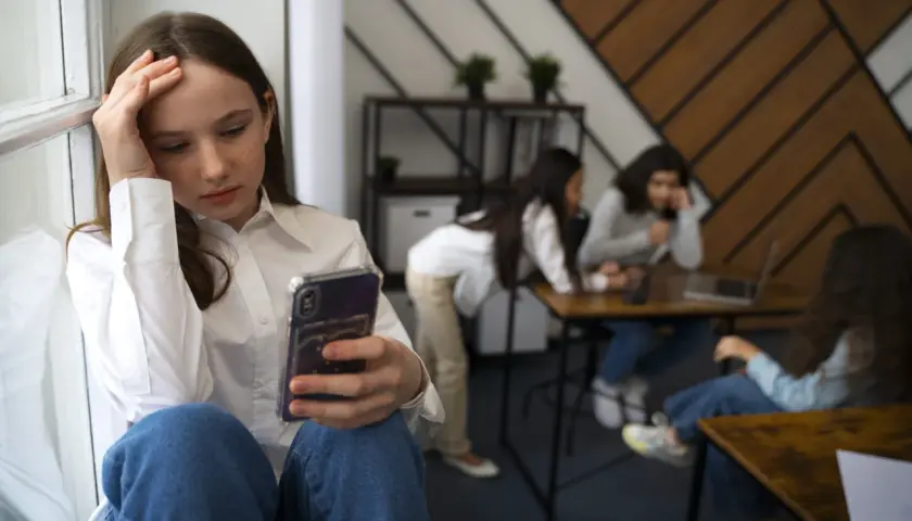 Dziewczyna z telefonem w dłoni, zmartwiona, odizolowana od grupy rówieśników. To obraz nieleczonej fobii społecznej.