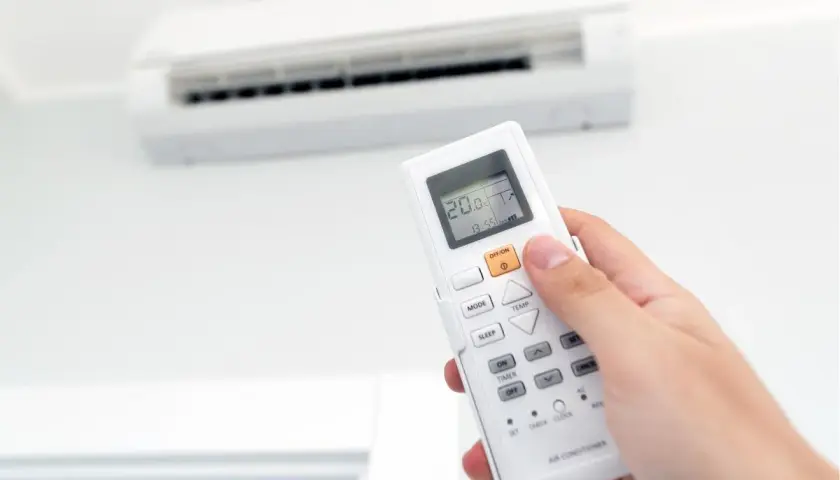 Mano sujetando un control remoto de aire acondicionado, ajustando la temperatura para combatir el calor o el frío.