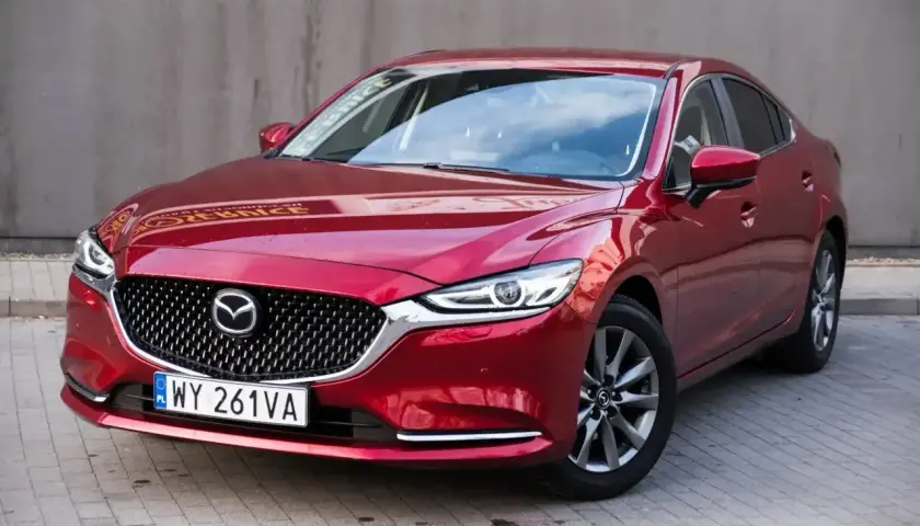 Czerwona Mazda 6 2.0 benzyna z polskimi tablicami rejestracyjnymi stoi na chodniku.