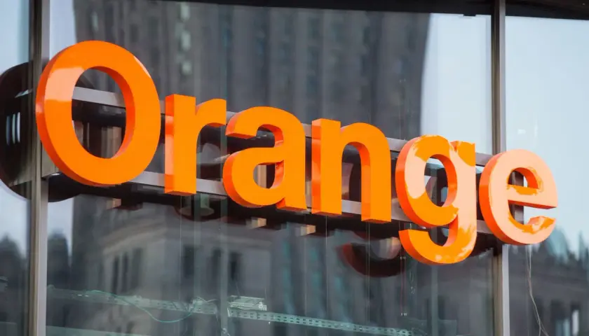 Pomarańczowe litery "Orange" na budynku. Firma ta oferuje usługi telekomunikacyjne, a jej nazwa kojarzy się z dobrymi zarobkami.