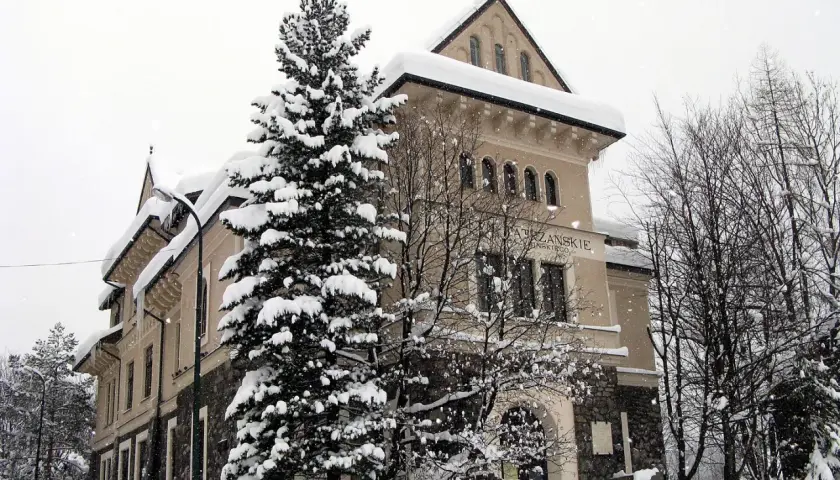Zimowy dzień w muzeum Tatrzańskiego Parku Narodowego. Śnieg otula drzewa i budynek, tworząc bajkową scenerię.