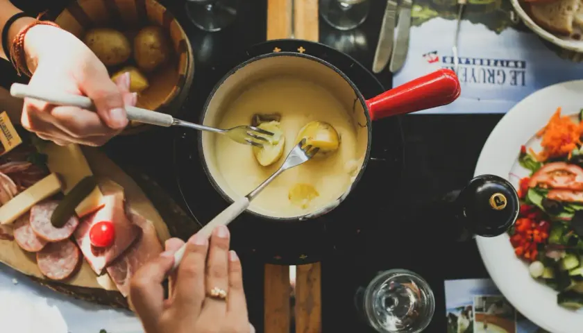 Des mains trempent des pommes de terre dans une fondue savoyarde, un délice de fromages fondus suisses.