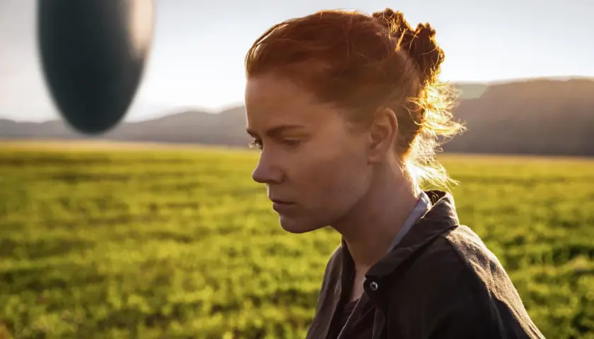 Donna con capelli rossi guarda un misterioso oggetto ovale fluttuante, simbolo dell'arrival linguaggio.