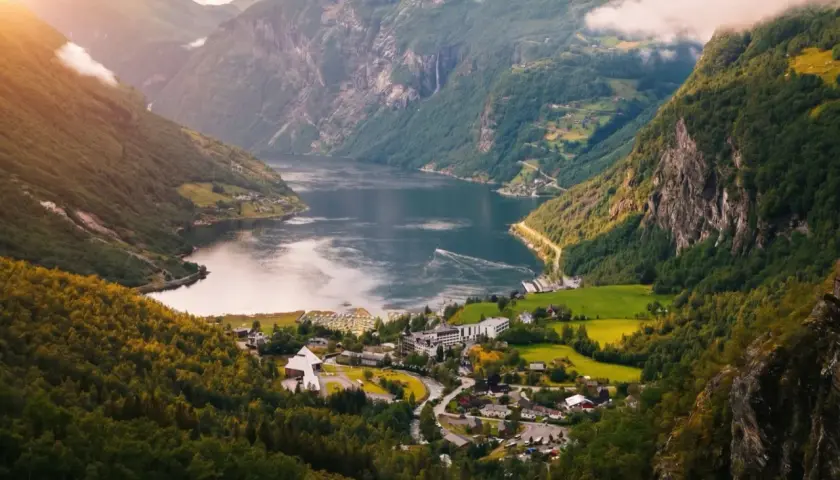 Malowniczy fiord w Norwegii, z zielonymi zboczami gór, wodospadami i małą wioską. Klimat tego miejsca sprzyja podziwianiu natury.