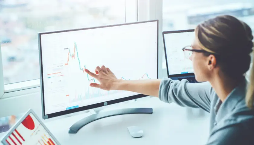 Kobieta analizuje wykres Sunex na monitorze, wskazując palcem na trend wzrostowy. Obok leży tablet z podobnymi danymi.