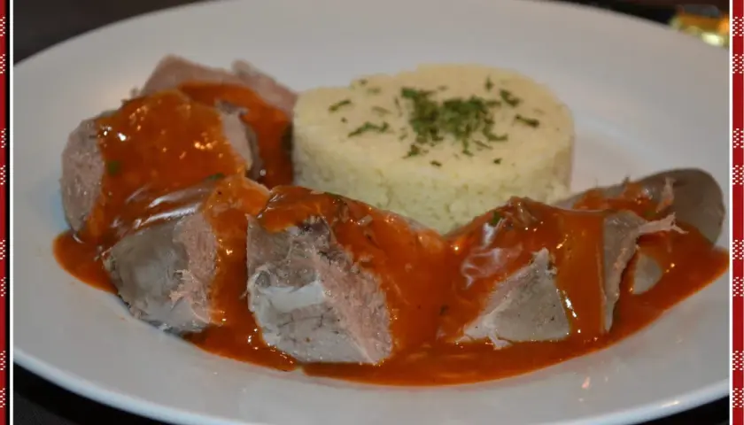 Langue de porc en sauce tomate, servie avec une portion de semoule garnie d'herbes. Un plat savoureux de "la cuisine de Lilly".
