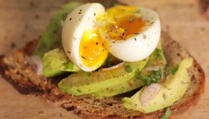 Tartine oeuf et avocat, un délice crémeux avec un jaune coulant, garnie d'herbes fraîches et d'épices sur du pain grillé.