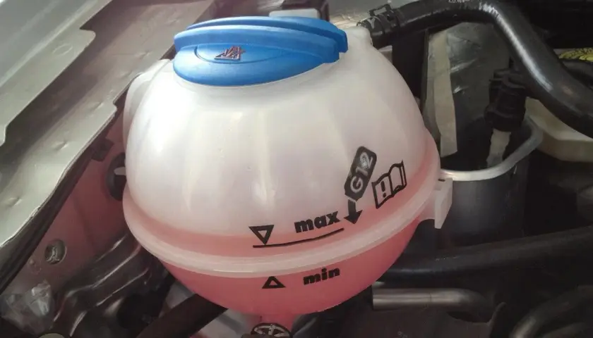Depósito de refrigerante con líquido rosa. Indica que agua se le echa al coche, entre los niveles "min" y "max", y especifica el tipo G12.