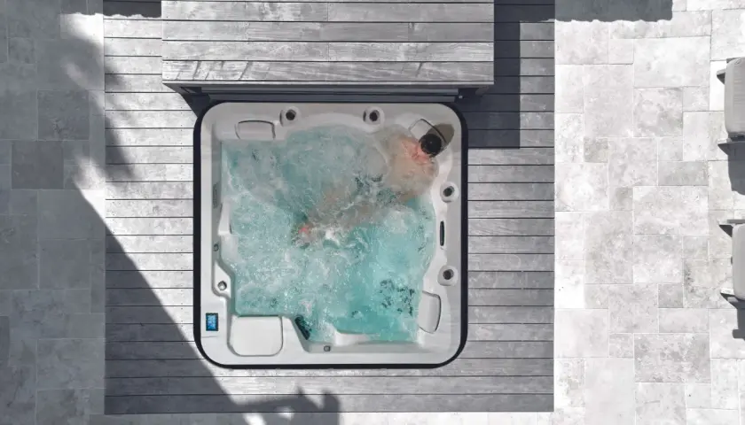 Un homme profite d'un traitement spa relaxant dans un jacuzzi bouillonnant, entouré de bois et de pierre.