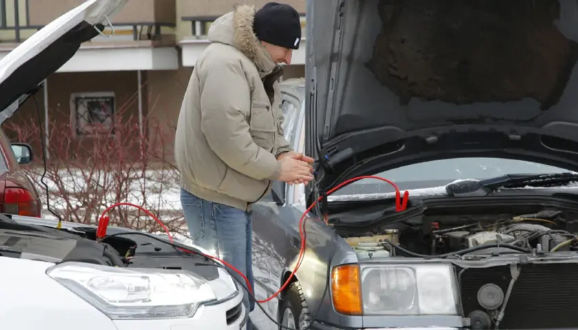 Mężczyzna próbuje odpalić auto zepsutym rozrusznikiem, używając kabli rozruchowych.