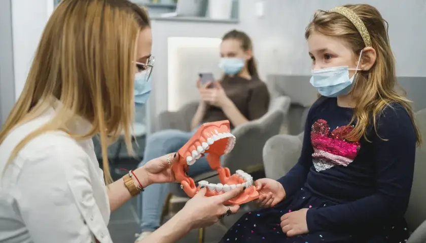 Ortodonta wyjaśnia dziecku budowę szczęki na modelu. W poczekalni siedzą inne osoby.