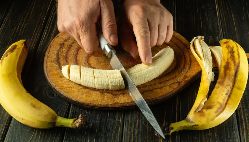 Dłonie kroją banana na desce. To świetny pomysł, co jeść na skurcze nóg, bo banany są bogate w potas.
