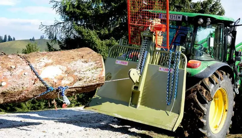 Ein Traktor mit einer **seilwinde** zieht einen Baumstamm aus dem **Wald**.