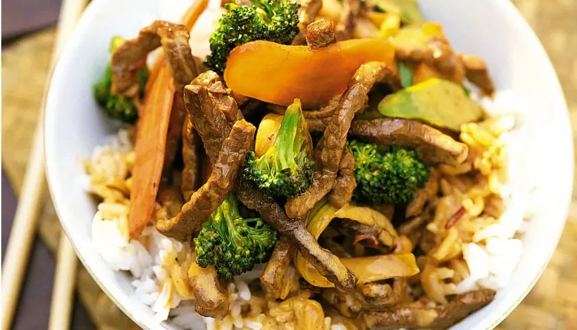 En skål med ris toppad med strimlad biff teriyaki, broccoli och morötter. En härlig asiatisk rätt.