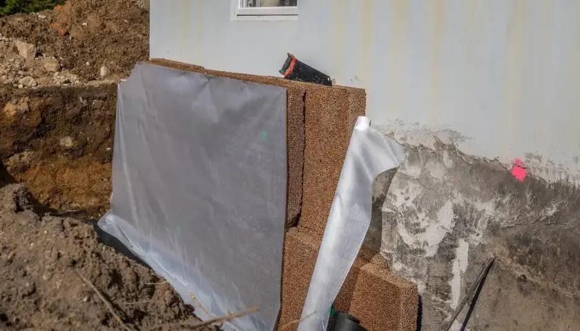 Byggarbetsplats där man ska isolera plintar med dränerande material och skyddande duk.