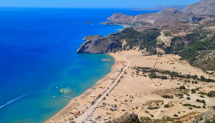 Malownicze plaże Rodos z turkusową wodą, leżakami i wodnym parkiem rozrywki. Widok z góry na wybrzeże i górzysty krajobraz.