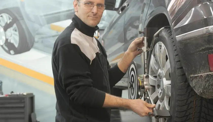 Mekaniker justerar hjulinställningen på en bil. Han ser till att allt är perfekt för att serva bilen.