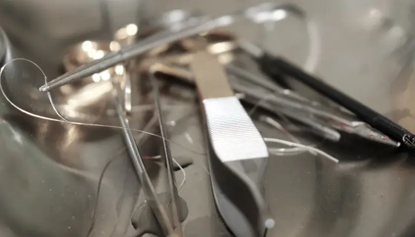 Pinces chirurgicales et fils de suture dans un plateau métallique. Un fil semble détaché, évoquant un point de suture qui a sauté après une circoncision.