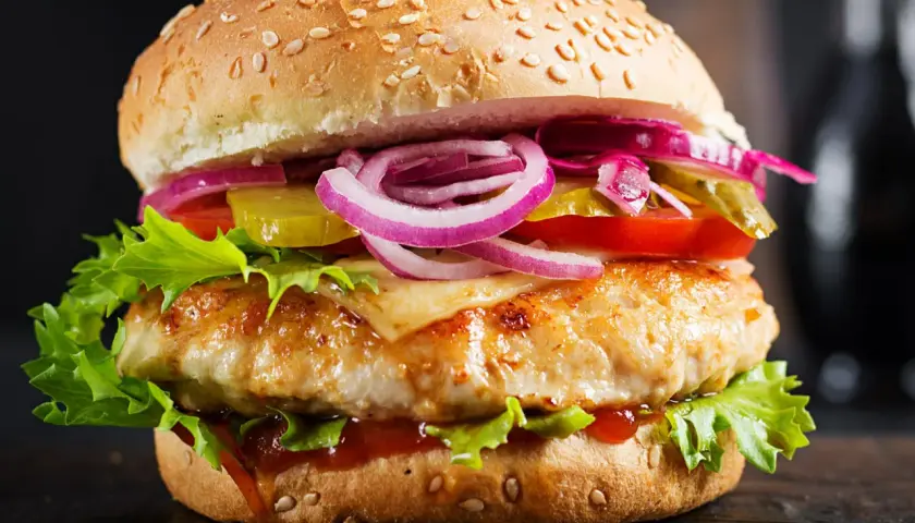 Makro zbliżenie na soczystego burgera drwala: grillowany kotlet, ser, sałata, pomidor, ogórek, czerwona cebula i sos na sezamowej bułce.