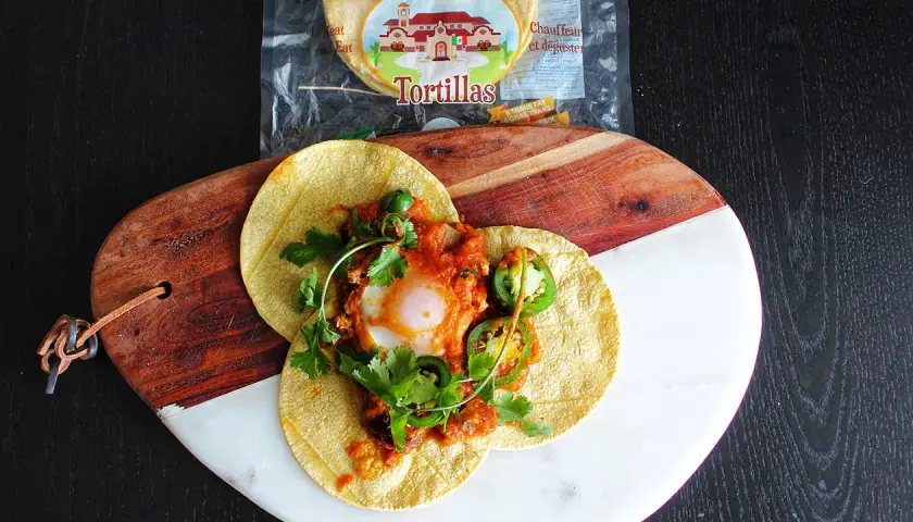 Délicieux huevos rancheros recette sur tortillas, garni d'un œuf coulant, sauce tomate épicée, jalapeños et coriandre fraîche.