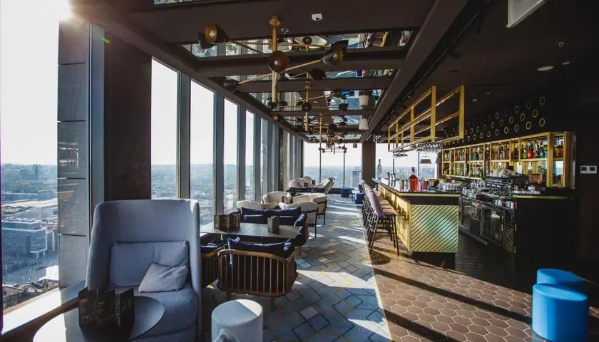 Nowoczesna restauracja z widokiem na miasto, z barem i wygodnymi fotelami.
