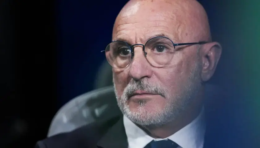 Łysy mężczyzna w okularach, z siwą brodą, w garniturze i krawacie. To trener reprezentacji Hiszpanii.