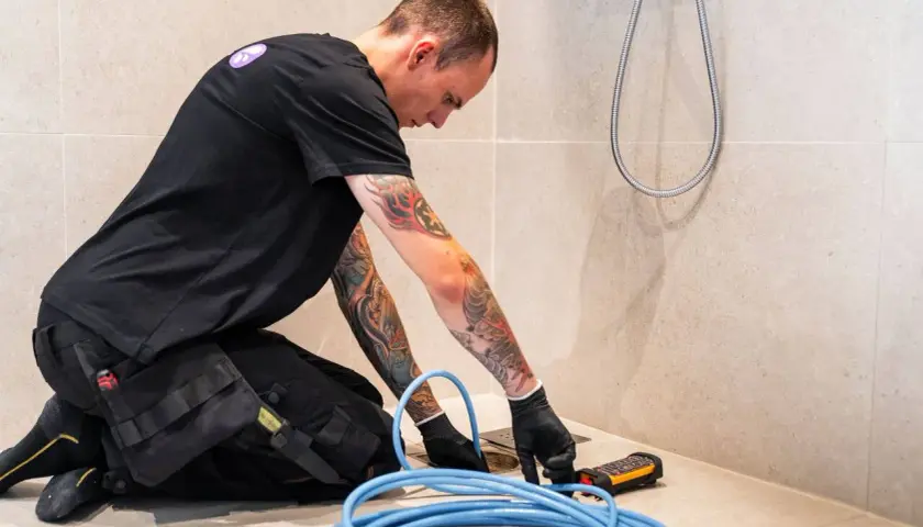 En rörmokare med tatueringar arbetar med en spolbil. Kostnad för spolbil kan variera beroende på problem.