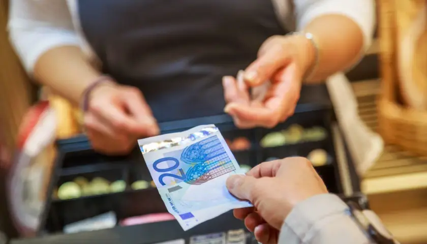 Une main tend un billet de 20 euros pour une saisie avoir espèces. Une caisse enregistreuse est visible en arrière-plan.