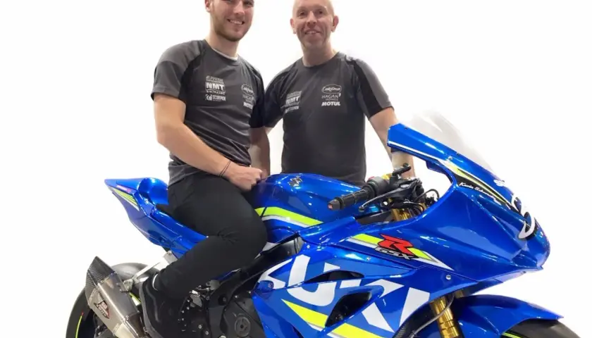Davey Todd y su equipo posan junto a una moto Suzuki azul brillante.