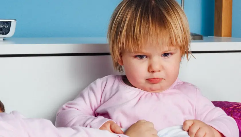 Smutna dziewczynka z nietolerancją laktozy u dzieci, siedzi w łóżku, czuje się źle po wypiciu mleka.