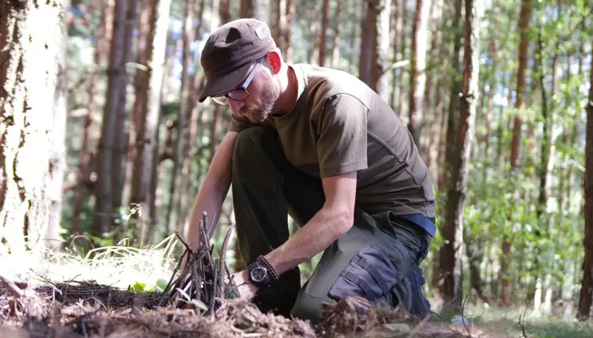 Mężczyzna w lesie przygotowuje rozpałkę do ogniska. To przykład, jak radzić sobie w trudnych warunkach, czyli survival co to znaczy w praktyce.