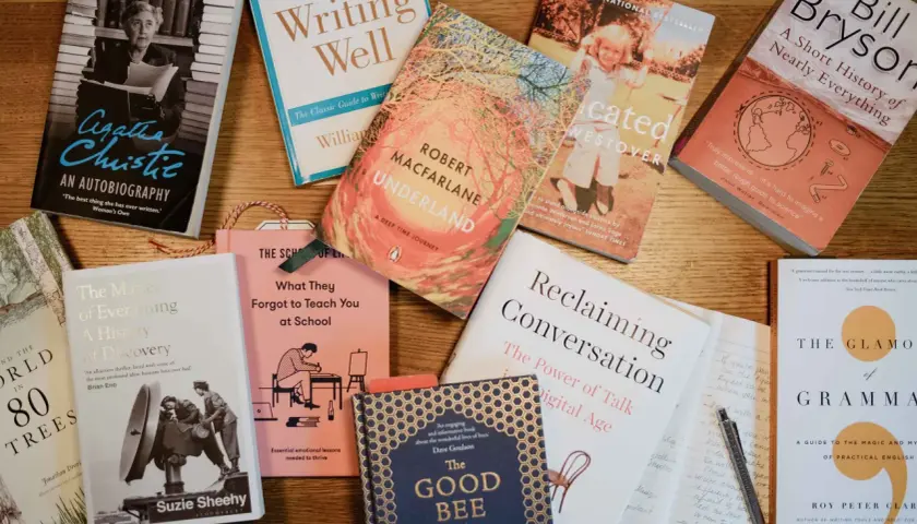 Une pile de livres sur une table en bois, parfaite pour un podcast littéraire. On y trouve des biographies, des essais et des romans.
